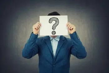 A person in a blue suit holds a paper with a large, hand-drawn question mark in front of their face, obscuring their identity, while pondering the nuances of an inbound marketing strategy against a gray background.