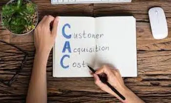 A person is meticulously noting the lower Customer Acquisition Cost, abbreviated as CAC, in their notebook. The wooden desk hosts a plant, keyboard, and mouse nearby. With pen in hand, they emphasize the word "Customer," underscoring their focus on reducing expenses.